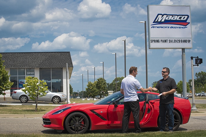 a couple of men standing next to a red sports car